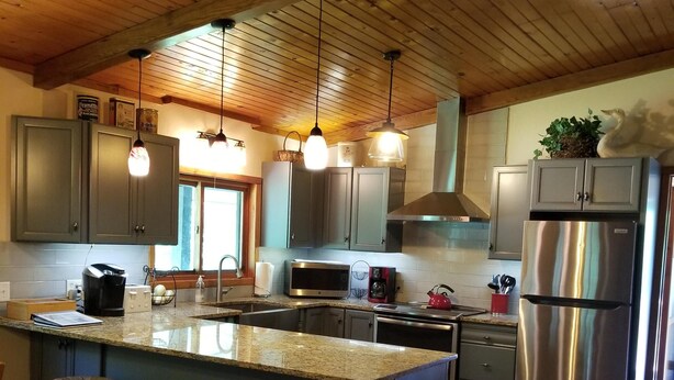 A modern kitchen with a central island, stainless steel appliances, and wooden ceiling beams. - Kettle River Cabin nestled between the Twin Cities & Duluth, MN (Hinckley)