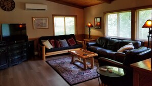 A cozy living room with a wooden ceiling, two sofas, a coffee table, a TV, and a fireplace. - Kettle River Cabin nestled between the Twin Cities & Duluth, MN (Hinckley)