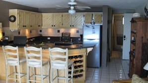 A kitchen with wooden cabinets, a central island with bar stools, a refrigerator, and a ceiling fan. - Beachfront Condo, Summer Special, 154 u.s.  per night!!!!!!! (Beauna Vista)