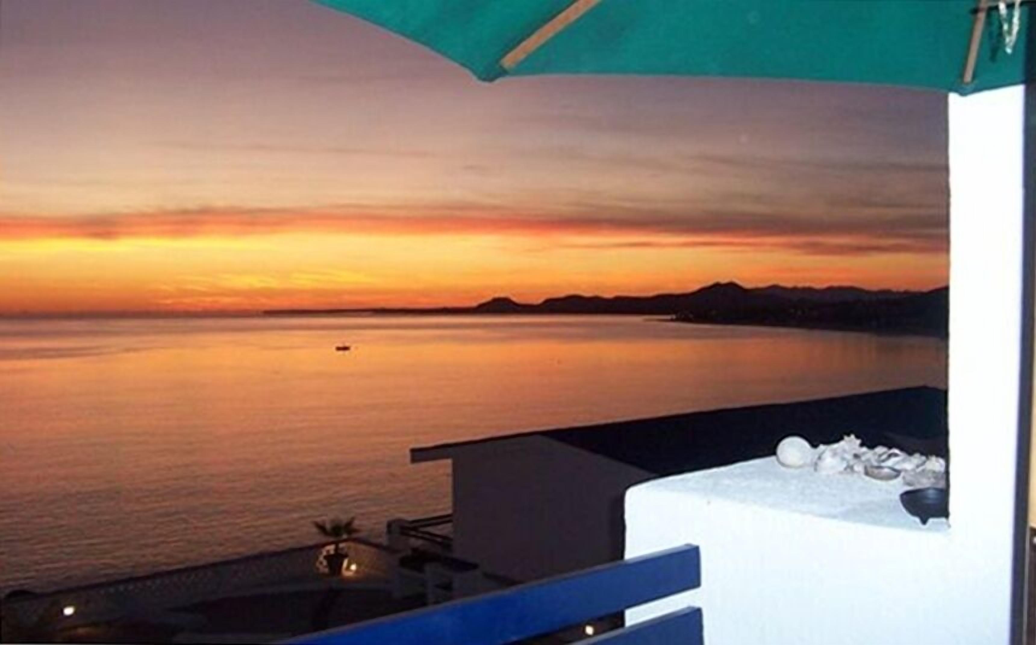 A sunset view from a balcony with a pool and a mountain in the distance.