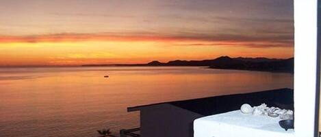 A sunset view from a balcony with a pool and a mountain in the distance.
