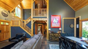 A spacious living area with a high ceiling, a staircase leading to an upper level, a dartboard, and a bar area.