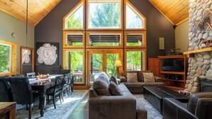 A spacious living area with a high ceiling, large windows, a fireplace, and a stone wall.