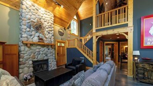 A cozy living room with a stone fireplace, a wooden staircase, and a comfortable seating area.