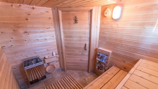 Een houten sauna met een bank, een sauna-oven en een klein plankje met spullen.