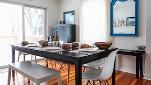 Een eetruimte met een houten tafel gedekt voor vier personen, witte stoelen, een donker houten kast en een spiegel met blauwe lijst aan de muur.
