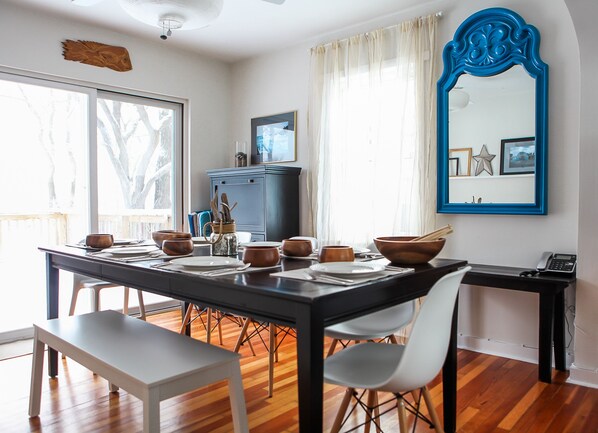 A dining area with a wooden table set for four, white chairs, a dark wooden cabinet, and a blue-framed mirror on the wall.