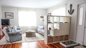 Een moderne woonkamer met een grijze bank, een witte fauteuil, een televisie en een boekenkast.