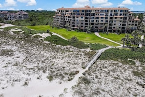 Un hotel de varios pisos con un patio central, rodeado de dunas de arena y vegetación.