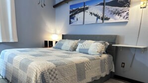 A bedroom with a bed, a nightstand, a wall-mounted shelf, and a painting of a snowy landscape.
