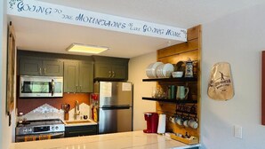 A kitchen with green cabinets, stainless steel appliances, a marble countertop, and a sign above stating 'Going to the Mountains is like Going Home.'