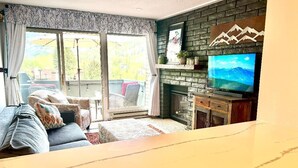 A living room with a sofa, a television, a fireplace, and a large window.