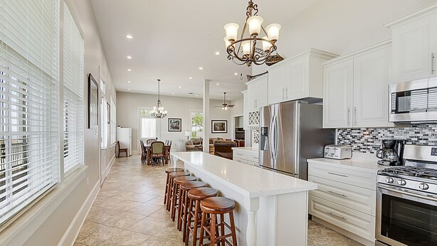 A modern kitchen with white cabinetry, a central island with bar stools, stainless steel appliances, and a chandelier. - LAKE House with Private Heated Pool, Great for Family Gatherings. Best View! (Slidell)