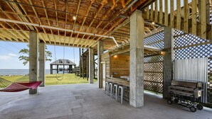 An outdoor covered patio with a grill and seating area, overlooking a grassy area and a building. - LAKE House with Private Heated Pool, Great for Family Gatherings. Best View! (Slidell)