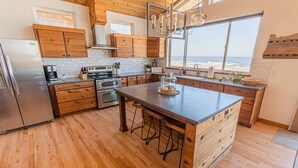 A modern kitchen with wooden cabinets, a stainless steel refrigerator, and a large island with stools. - Ocean Views for days.....Oceanfront property that will leave you breathless! (Cloverdale)