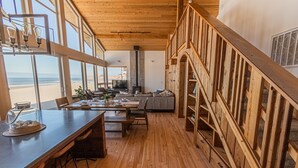 A spacious room with a wooden floor, a dining area with a table and chairs, a sofa, and a large window overlooking the beach. - Ocean Views for days.....Oceanfront property that will leave you breathless! (Cloverdale)