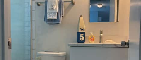 Un baño con inodoro, lavamanos con espejo, toallero y cubo de basura.
