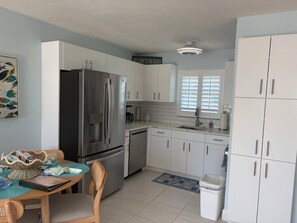 Eine moderne Küche mit weißen Schränken, einem Edelstahl-Kühlschrank, einer Kaffeemaschine und einem Essbereich mit Tisch und Stühlen.