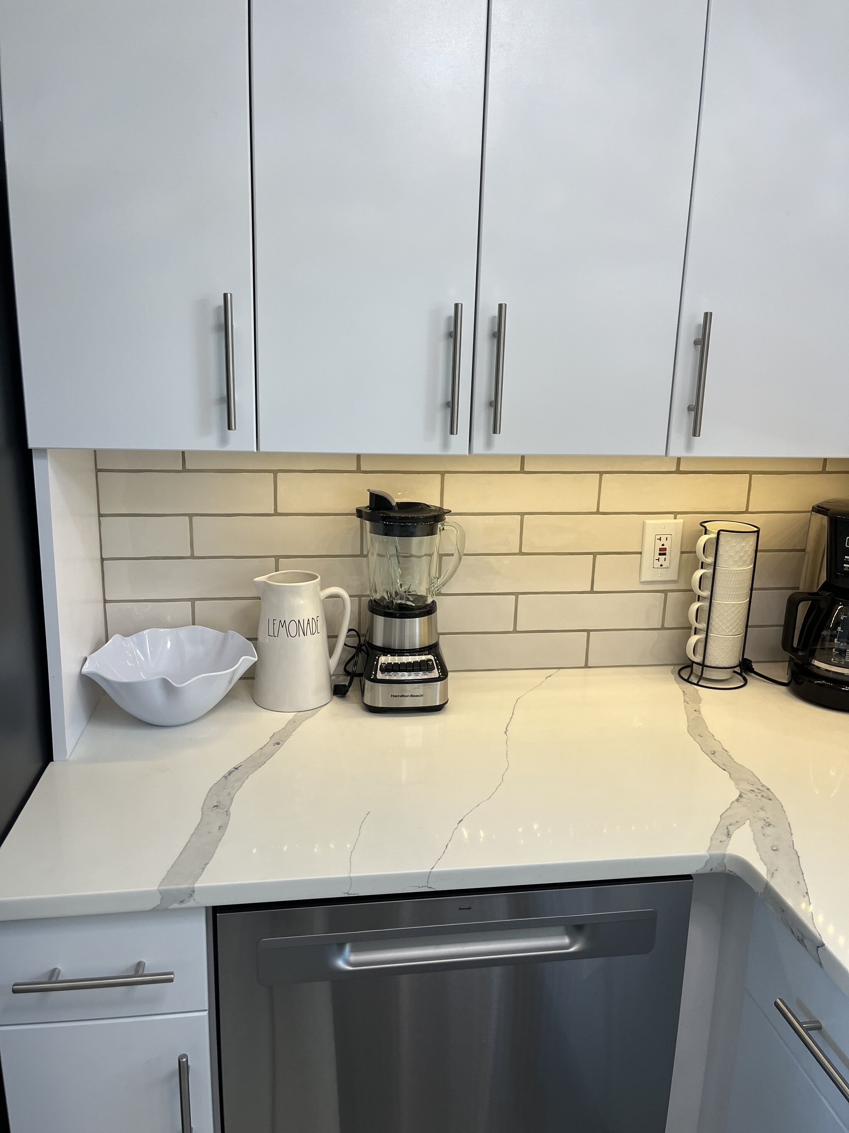 Eine Küche mit weißen Schränken, einem Mixer, einer weißen Tasse und einer Kaffeemaschine.