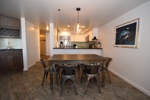 Une cuisine moderne avec une table et des chaises en bois, un luminaire suspendu et un tableau encadré au mur.