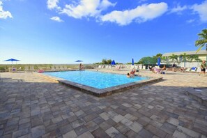 Une piscine dont le fond est recouvert de carrelage, entourée de chaises longues et de parasols.