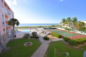 A hotel with a swimming pool, tennis court, and a view of the beach.