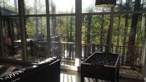 Una habitación con mesa de fútbol, sofá de cuero y vistas a una terraza con mobiliario exterior y barandilla.