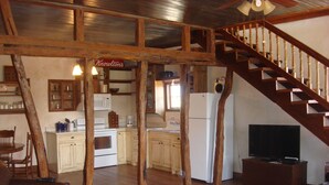 Une cuisine rustique avec des poutres en bois, un escalier en bois et un coin repas agrémenté d’un canapé en cuir.