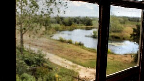 Une fenêtre donnant sur un paysage naturel, comprenant une étendue d’eau et de la végétation.