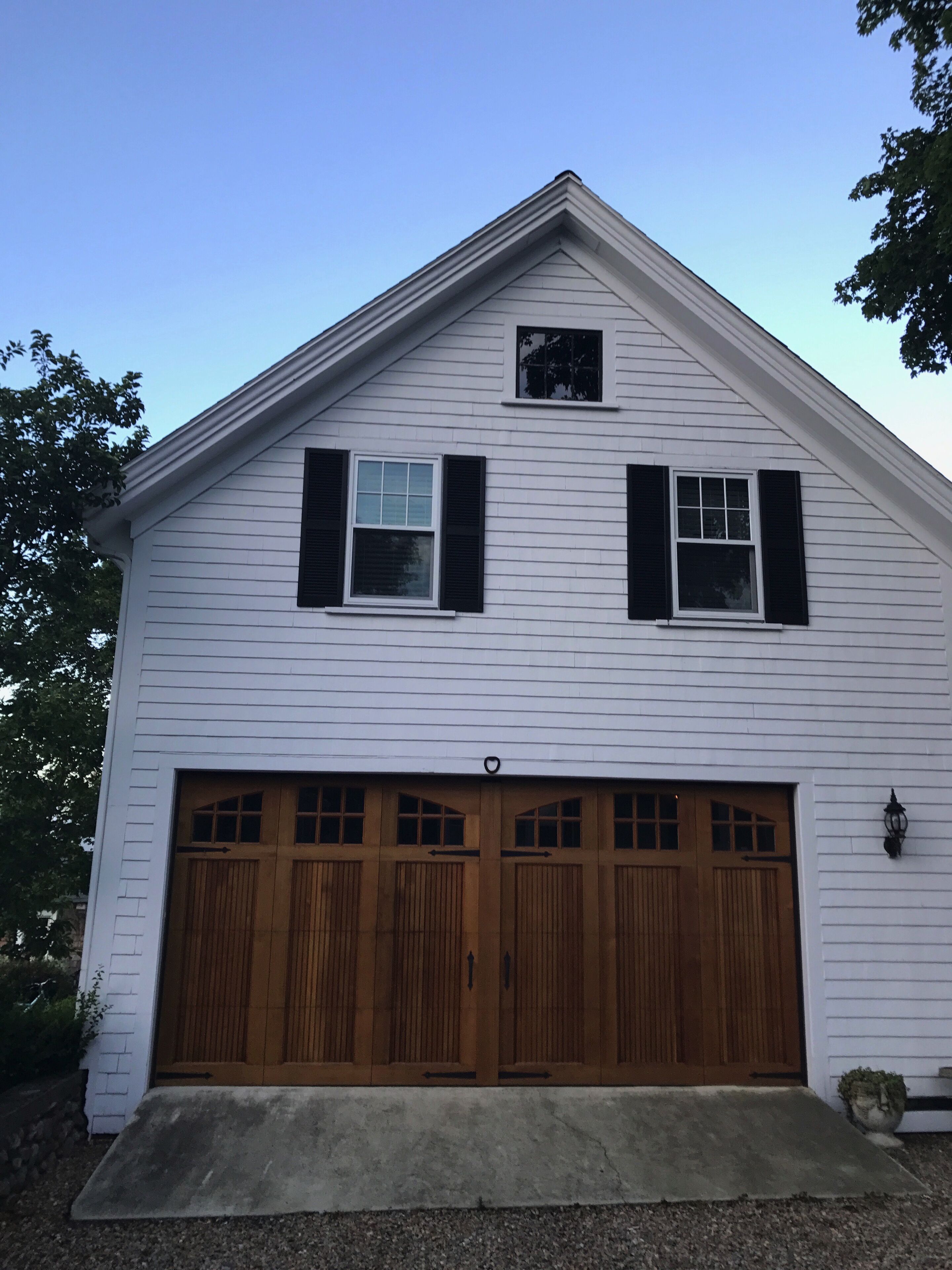 A two-story white building with a gabled roof, a garage with wooden doors, and a small window on the upper floor.