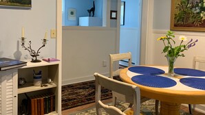 A dining area with a round table, chairs, a vase with flowers, and a bookshelf with books. - Discover Coastal charm, just a quick 26-min drive away (Damariscotta)