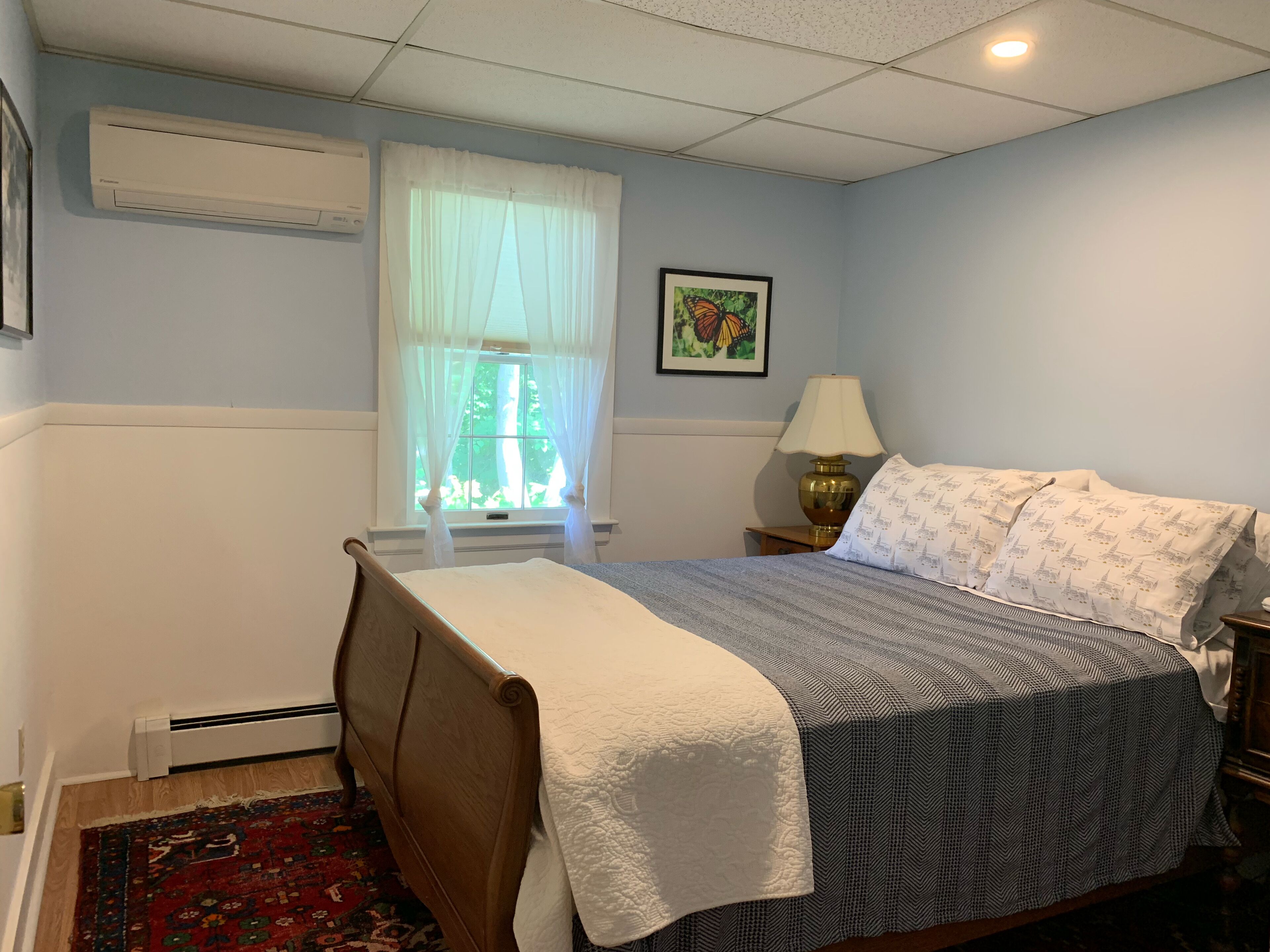A bedroom with a bed, a window with curtains, a nightstand, a lamp, and a framed picture on the wall.