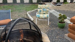 A backyard with a stone fire pit, outdoor seating, and a small garden area. - Discover Coastal charm, just a quick 26-min drive away (Damariscotta)