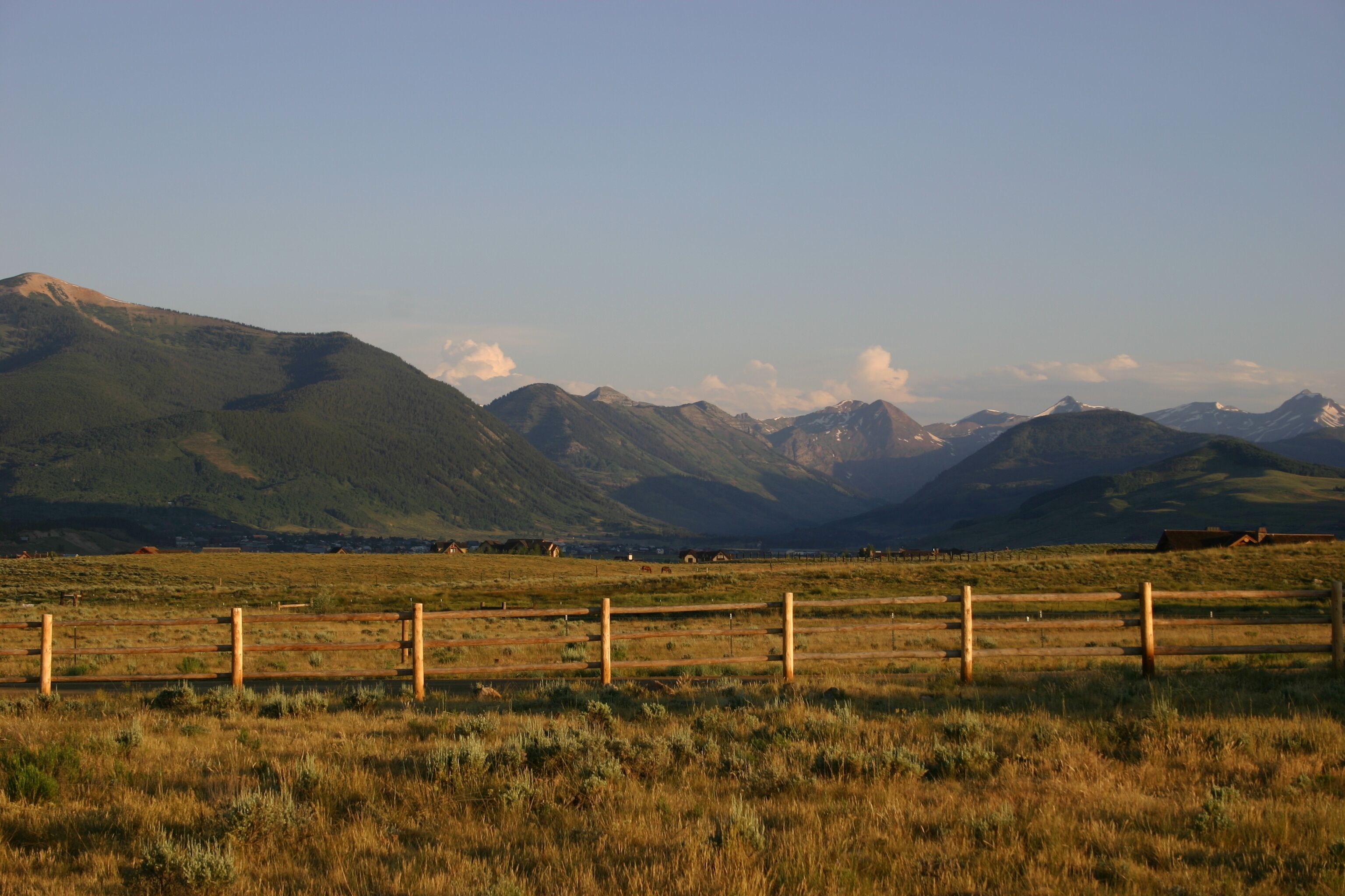 A rural landscape with mountains in the background, a wooden fence in the foreground, and a clear sky.