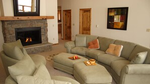 A living room with a stone fireplace, a sectional sofa, and an ottoman with snacks. - POSTCARD VIEWS-3 min TO TOWN, 5 TO SLOPES 10 ACRES 2100 SQFT  (Crested Butte)