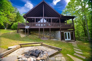 Surrounded by lush greenery, this cabin features a balcony, stone fire pit, and a blend of rustic and modern design elements.