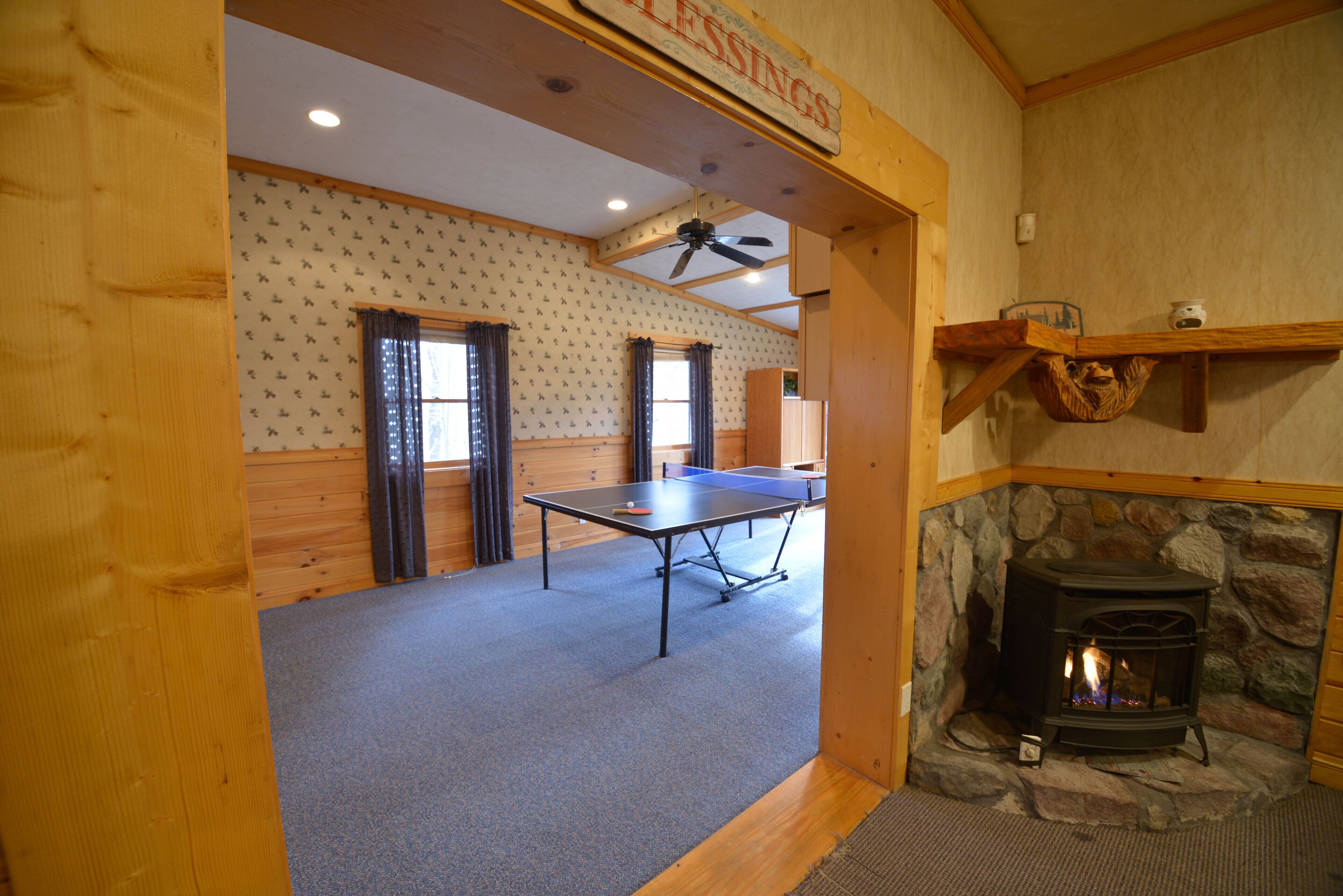 Una habitación con mesa de ping-pong, chimenea de piedra y ventilador de techo.