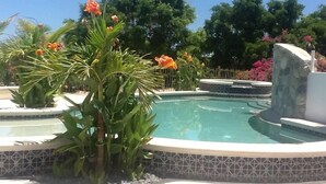 Una piscina con borde de azulejos, rodeada de abundante vegetación y plantas florecientes.
