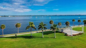 A waterfront view with a grassy area, palm trees, and a clear blue sky. - Water front, Bring Your Boat or drop a fishing line, enjoy a beautiful sunset ! (Punta Gorda)