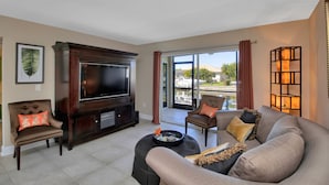 A living room with a large flat-screen TV, comfortable seating, and a view through a sliding glass door. - Water front, Bring Your Boat or drop a fishing line, enjoy a beautiful sunset ! (Punta Gorda)