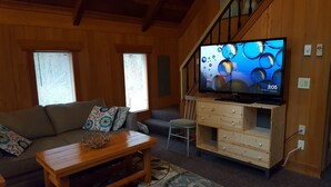 A cozy living room with a wooden staircase, a large flat-screen TV, a sofa, a coffee table, and a chair. - Enjoy a Relaxing Weekend in the Woods at Shady Maple Cottage🌲🍂🍁 (Hoodsport)