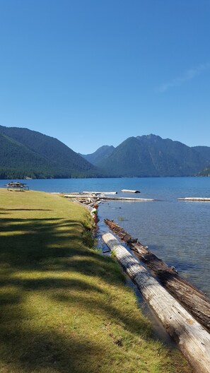 A lakeside view with a grassy area, a wooden dock, and mountains in the background. - Enjoy a Relaxing Weekend in the Woods at Shady Maple Cottage🌲🍂🍁 (Hoodsport)
