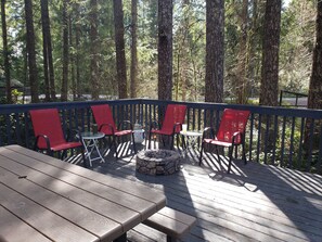 A wooden deck with a table and red chairs, surrounded by tall trees. - Enjoy a Relaxing Weekend in the Woods at Shady Maple Cottage🌲🍂🍁 (Hoodsport)