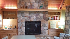 A cozy room with a stone fireplace, a dining table with chairs, a striped armchair, and a bookshelf filled with books. - Enjoy a Relaxing Weekend in the Woods at Shady Maple Cottage🌲🍂🍁 (Hoodsport)