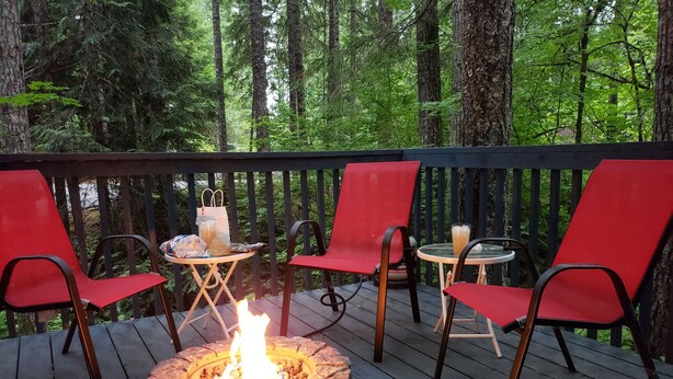A deck with a stone fire pit, red chairs, and a small table with a drink. - Enjoy a Relaxing Weekend in the Woods at Shady Maple Cottage🌲🍂🍁 (Hoodsport)