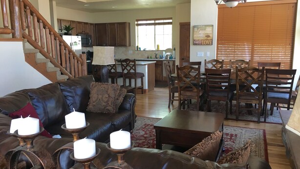 Un salón espacioso con un sofá de cuero, una zona de comedor con sillas de madera, una cocina al fondo y una escalera que sube a otro nivel.