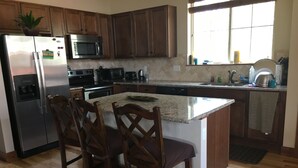 Una cocina con armarios de madera, un refrigerador de acero inoxidable, un microondas, una estufa y un lavamanos.