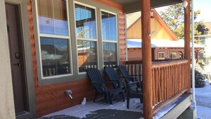 Una cabaña de madera con porche, tres sillas Adirondack y una terraza cubierta de nieve.