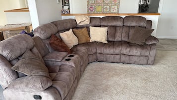A sectional sofa with a built-in recliner, a small table, and a decorative wall hanging.