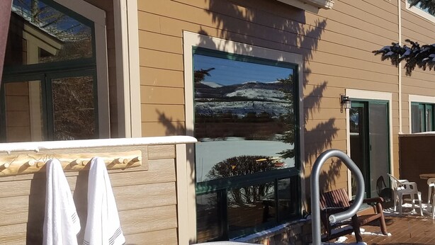 Una vasca idromassaggio con vista su un paesaggio innevato, un patio coperto e un edificio con facciata beige e finestre blu.